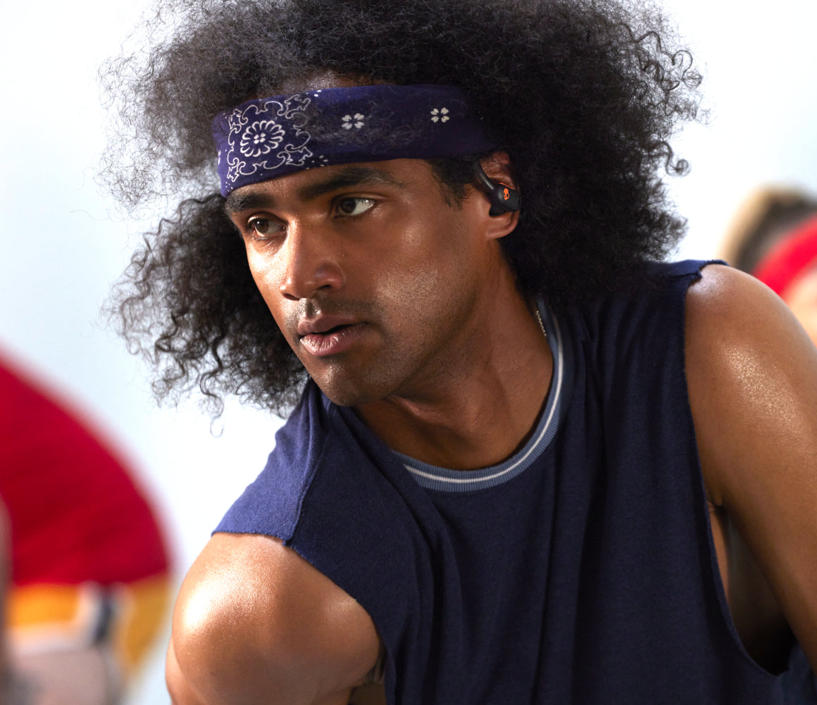 Young man in a tank-top and bandana listening to music with  Skullcandy wireless sport earbuds with flexible ear hooks